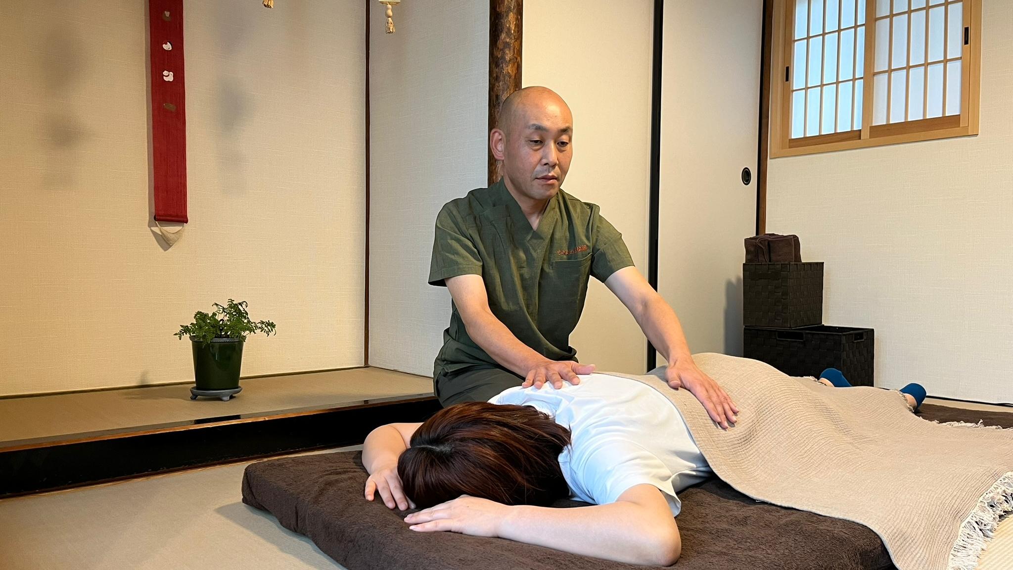 Usui Reiki session in a serene tatami room, practitioner placing hands on client's back for relaxation and energy balance.